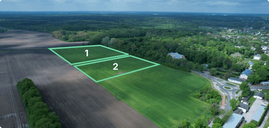 Widok z drona na dwie sąsiadujące działki oznaczone numerami 1 i 2, położone wśród zielonych terenów i zabudowy.